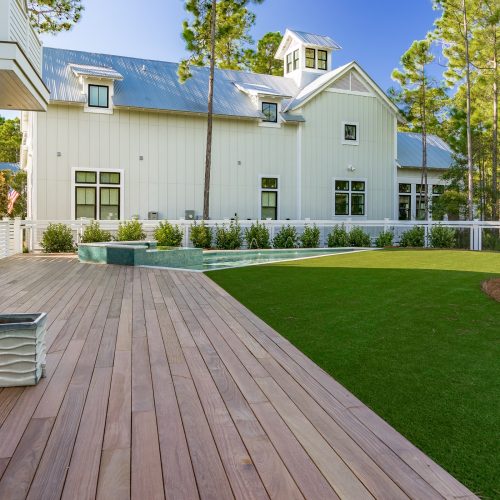 The backyard of a modern home features a long wooden deck and green grass.