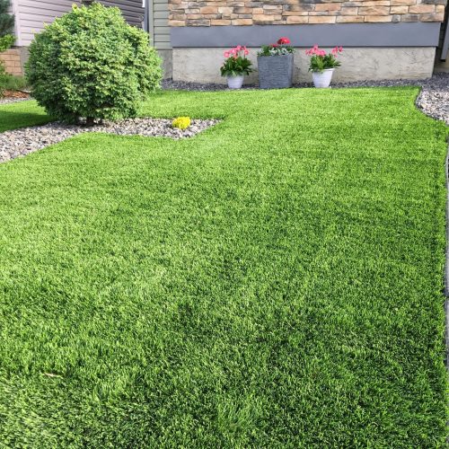 A beautiful artificial lawn in the front yard with nice flowers and shrubs surrounding it