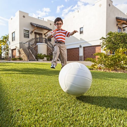 A 5 year old boy kicks a ball on artificial grass.
